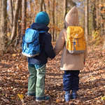 Finkid Kinder Outdoor Rucksack seaport/navy Wasser und Schmutz abweisend_29108 Zwei Kinder mit Finkid Kinder Outdoor Rucksack in seaport/navy warm angezogen halten sich an den Händen während sie auf einem laubbedeckten Waldweg im Herbstsonnenlicht spazieren gehen. Der Rucksack ist wasser- und schmutzabweisend.