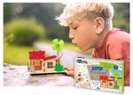Ein junger blonder Junge bläst auf ein kleines Haus mit einem grünen Windrad aus dem Moses. Verlag Bausatz Windrad im Freien auf Stein gesetzt. Der Bausatz Windrad erscheint in der Ecke.