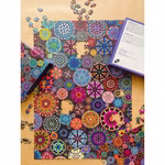 Das Penny Puzzle "Puzzle Mosaic Studio 1000 Teile" zeigt ein lebendiges kompliziertes kreisförmiges Mosaik das teilweise zusammengesetzt ist und dessen Teile und Kästchen auf einer hellbraunen Oberfläche verstreut sind.