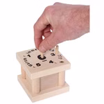 Bartl Warum immer ich? Würfelspiel_31722 Eine Hand hebt einen Holzpflock aus dem Bartl "Warum immer ich?" Würfelspiel - eine quadratische Schachtel mit nummerierten Löchern und Text auf der Oberseite die an ein Puzzle oder Lernspiel erinnert.