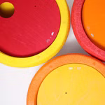 Grimm's GRIMM’S x Stapelstein® Kullerscheiben rot gelb orange _31800 Drei farbenfrohe GRIMM'S x Stapelstein® Kullerscheiben (rot gelb orange) von Grimm's jeweils mit Schaumstoffrand und Holzkern sind dicht an dicht auf weißem Grund angeordnet. Kleine Piktogramme und Plus-Minus-Symbole zieren die Oberflächen.