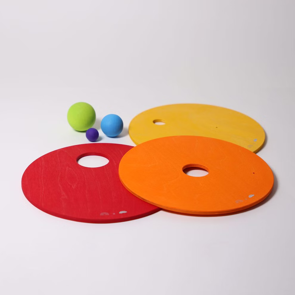 Grimm's GRIMM’S x Stapelstein® Kullerscheiben rot gelb orange _31796 Drei GRIMM'S x Stapelstein® Kullerscheiben aus Holz in Rot Gelb und Orange von Grimm's sind auf einer weißen Fläche angeordnet daneben liegen vier Kugeln in Grün Blau Lila und Hellblau.