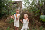 Grapat Grapat Serendipity Stapelturm _32156 Zwei kleine Kinder in heller Kleidung spielen im Freien im Grünen. Ein Kind balanciert einen Stapel Grapat Serendipity Stapeltürme von Grapat während das andere aufgeregt zusieht. Im Hintergrund steht ein altes Steinbauwerk.