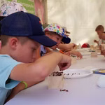 Kinder mit bunten Mützen sitzen an einem Tisch und verzieren Holzschatztruhen mit Trommelsteinen mit dem "Bastelset Schatztruhe mit Trommelsteinen gestalten & kleben" von Maulwurf - Geschenke aus der Natur. Sie sind konzentriert und kreativ bei ihrer Baste