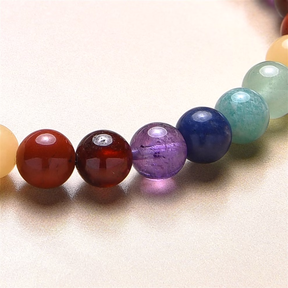 Marco Schreier Mineralienhandlung GmbH Kinder-Chakra-Armband Länge 15 cm_32729 Eine Nahaufnahme des farbenfrohen Kinder-Chakra-Armbandes (15 cm) der Marco Schreier Mineralienhandlung GmbH mit geschliffenen Edelsteinperlen in den Farben Rot Lila Blau Grün und Gelb die auf einer glatten hellen Oberfläche angeordnet sind.