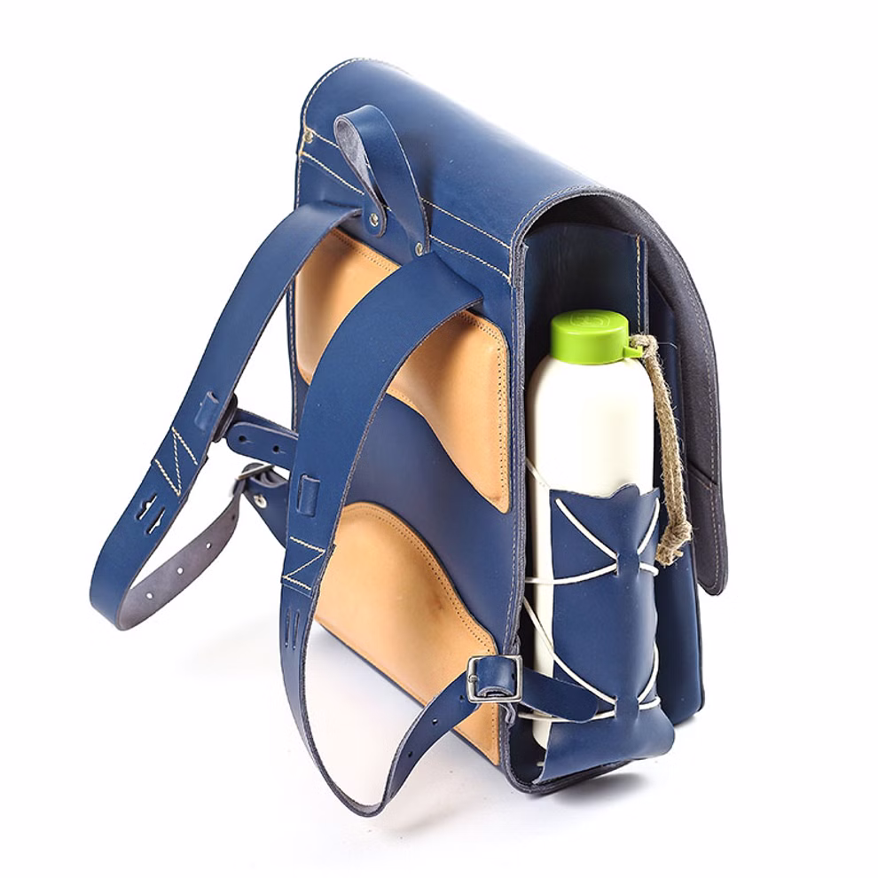 hukkepack Schulranzen Leder Blau Kompakt _32597 Der hukkepack Schulranzen Leder Blau Kompakt Rucksack hat gepolsterte Träger und Rücken eine Seitentasche mit einer weißen Flasche mit grünem Deckel abgebildet auf weißem Hintergrund.