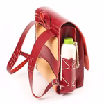 Der hukkepack Schulranzen Leder Rot Kompakt ist ein rot-hellbrauner Lederrucksack mit zwei Schulterriemen und einer Seitentasche in der eine weiße Flasche mit grünem Verschluss aufrecht auf weißem Hintergrund steht.