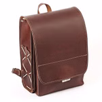 hukkepack Schulranzen Leder Braun Kompakt _32609 Der "Schulranzen Leder Braun Kompakt" von hukkepack ist ein brauner Lederrucksack mit weißen Nähten geprägtem Markennamen auf der Klappe und einer äußeren Seitentasche mit gekreuzten Riemen.