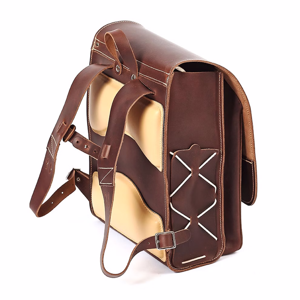 hukkepack Schulranzen Leder Braun Kompakt _32611 Der hukkepack Schulranzen Leder Braun Kompakt ist ein braun-hellbrauner Lederrucksack mit zwei Schulterriemen Ziernähten und einem Kreuzmuster auf dem Rücken dargestellt auf weißem Hintergrund.