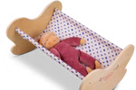 Käthe Kruse Waldorf Puppenwiege Holz_33047 Die Käthe Kruse Waldorf Puppenwiege Holz zeigt eine weiche Stoffpuppe in burgunderrotem Outfit und Strickmütze die in einer kleinen Holzwiege mit blau-weiß gemusterter Hängematte ruht.