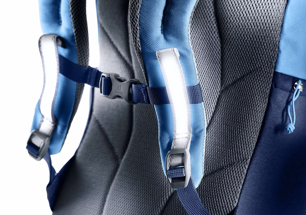 Deuter Deuter Waldfuchs Rucksack groß wave-nightblue Volumen 14 l_33395 Nahaufnahme des Deuter Waldfuchs Rucksack groß wave-nightblue (14L) mit gepolsterten Schultergurten mit Reflexstreifen und schwarzer Brustschnalle vor grauem und blauem Hintergrund.