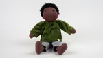 Dunkelhäutige Stoffpuppe mit kurzen schwarzen Locken, grünem Oberteil und heller Hose, sitzend vor weißem Hintergrund.