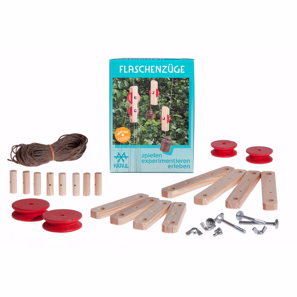 Kraul Bausatz Flaschenzüge _1508 Der Kraul Bausatz Flaschenzüge enthält Holzteile rote Flaschenzüge Schrauben Haken und braune Schnur die in einer Schachtel mit der Aufschrift "Bausatz Flaschenzüge" und einer Abbildung des zusammengebauten Flaschenzugsystems präsentiert werden.