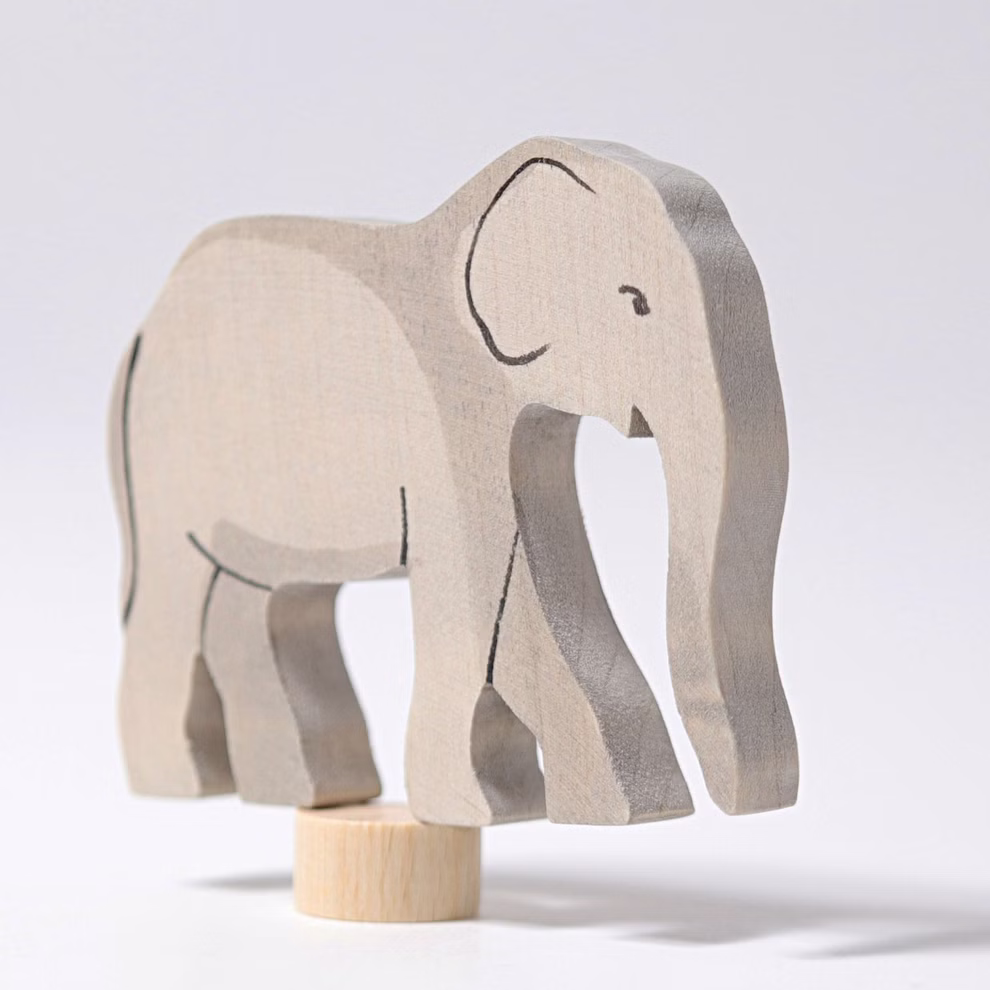 Der Grimms Geburtstagsstecker Elefant von Grimm's ist eine helle hölzerne Elefantenfigur mit einfachen schwarzen Linien die auf einem kleinen runden Sockel vor einem schlichten weißen Hintergrund steht.