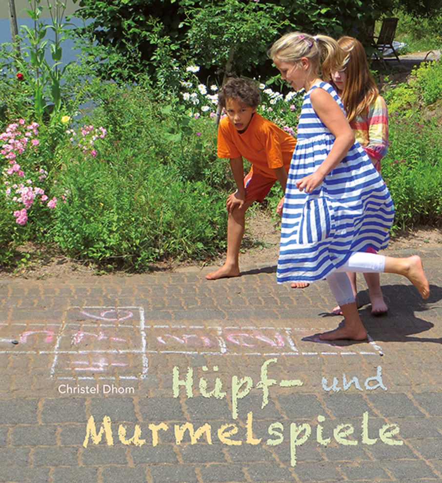 Freies Geistesleben Hüpf- und Murmelspiele Christel Dhom_22724 Drei Kinder vergnügen sich bei den Hüpf- und Murmelspielen Christel Dhom von Freies Geistesleben und spielen Himmel und Hölle auf einem sonnenbeschienenen Weg mit Kreidezeichnungen. Zwei Mädchen (eines in Streifen) und ein Junge in Orange bewegen sich inmi