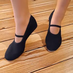 Eine Person steht auf einem Holzfußboden und trägt Morgenspruch Eurythmieversand Eurythmieschuhe Standard in schwarz mit einem einzelnen Riemen über jeden Fuß. 44