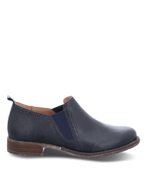 Mocassin élégant en cuir bleu marine avec un élastique confortable sur le côté. La chaussure a une semelle plate marron clair et des coutures discrètes sur les bords.