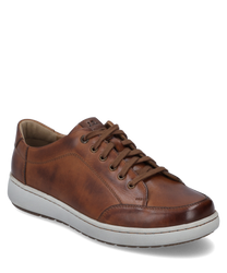 La sneaker en combinaison cognac présente une surface en cuir lisse avec des coutures claires et une semelle en caoutchouc blanche stable. Les caractéristiques particulières sont les lacets marron et la couture discrète qui donnent à la chaussure un look é