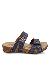 Die Sandale hat einen Klettverschluss und besteht aus einem blauen floral gemusterten Material. Besondere Merkmale sind die metallischen Blumenapplikationen auf den Riemen und die komfortable Korksohle.