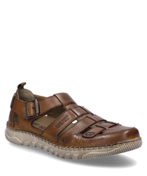 Una scarpa in pelle color cognac con una fibbia distintiva come chiusura. La scarpa ha una suola robusta e aree aperte che garantiscono ventilazione.