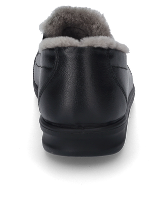 Una zapatilla de casa negra con un forro suave y un elástico como cierre. La zapatilla está hecha de material liso y ofrece una comodidad de uso agradable.
