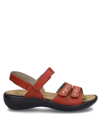 La sandalia es roja y cuenta con un práctico cierre de velcro. Tiene una suela cómoda y está adornada con elementos decorativos en las correas.