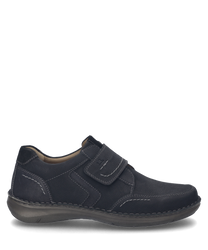 The shoe is black and made of a smooth material with visible seams. It features a practical Velcro closure for easy on and off.