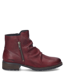La bota de cuero color burdeos cuenta con una cremallera lateral y pliegues decorativos en el lado exterior. El zapato tiene una suela plana con un ligero tacón ideal para una apariencia elegante y cómoda.