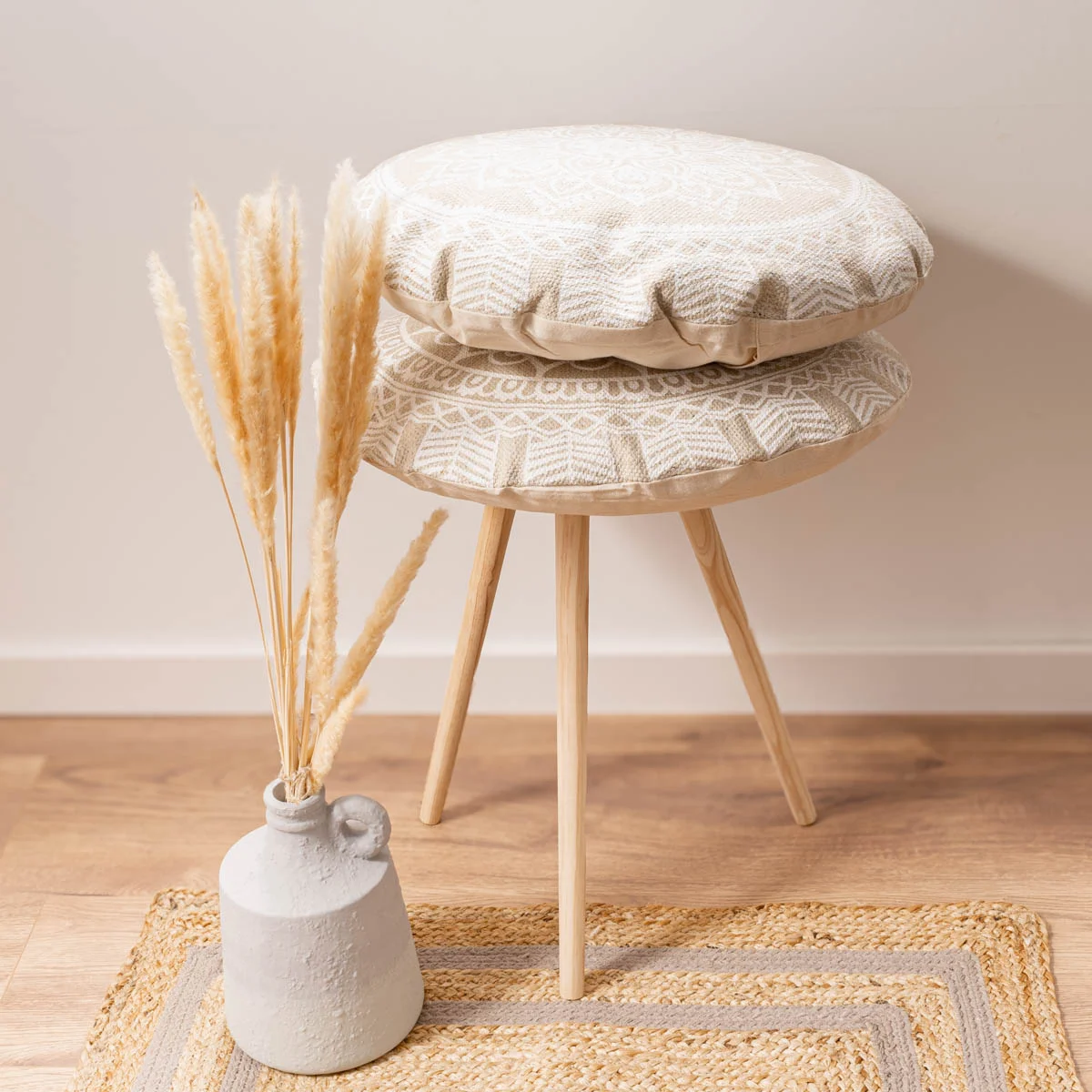 Zwei runde Kissen mit Mandala-Muster in Beige auf einem Hocker