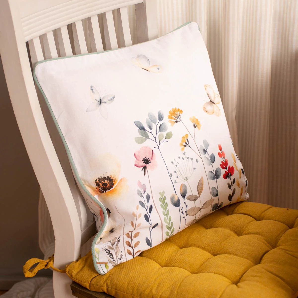 Buntes Kissen mit Blumen- und Schmetterlingsmotiv auf Stuhl mit gelbem Sitzkissen