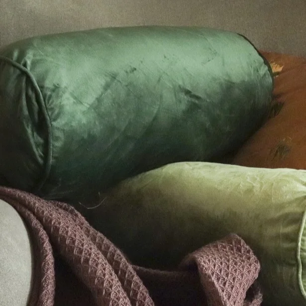 Gr&uuml;ne Samtkissen in verschiedenen Formen auf grauem Sofa