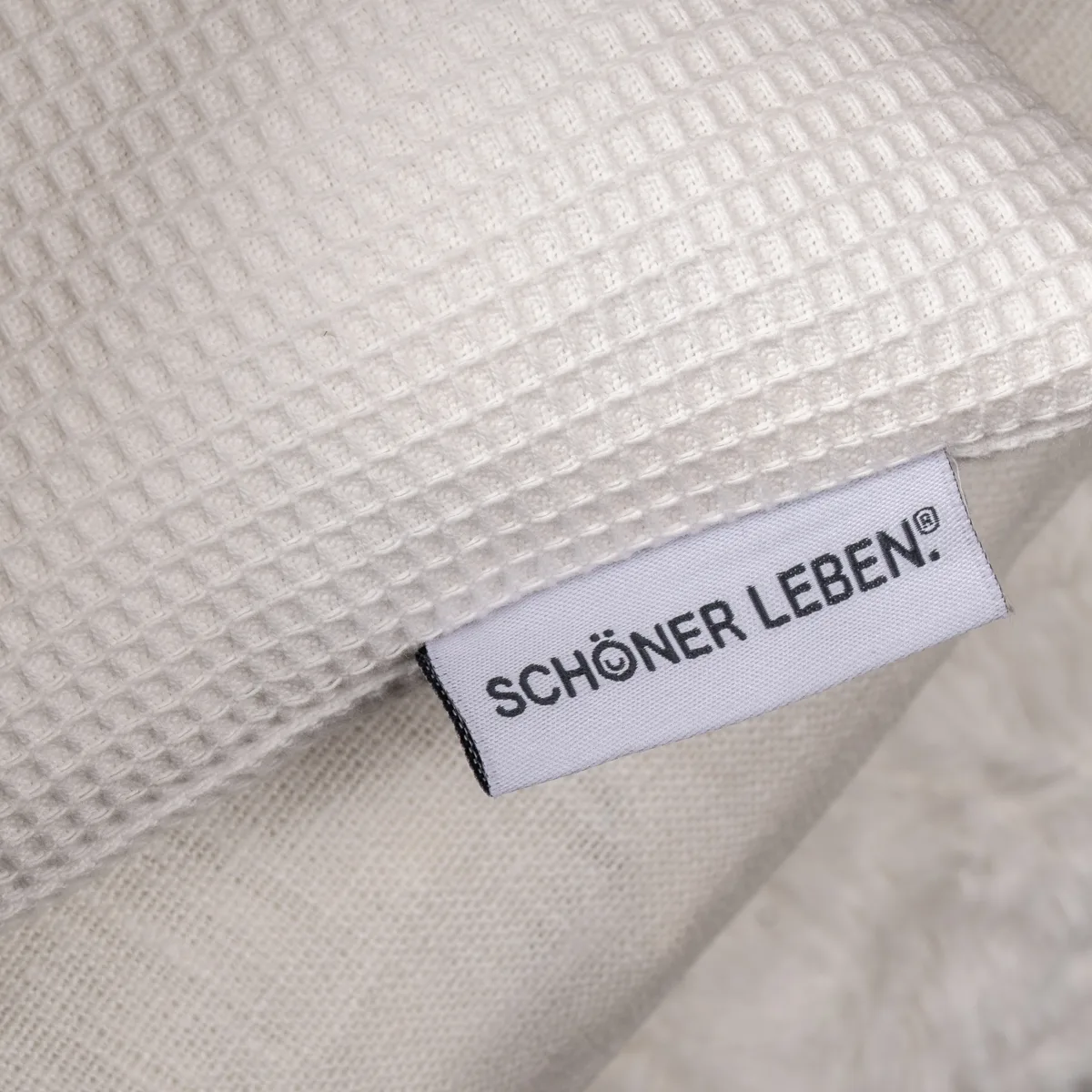 Wei&szlig;es Kissen aus Waffelpiqu&eacute; mit SCH&Ouml;NER LEBEN Etikett