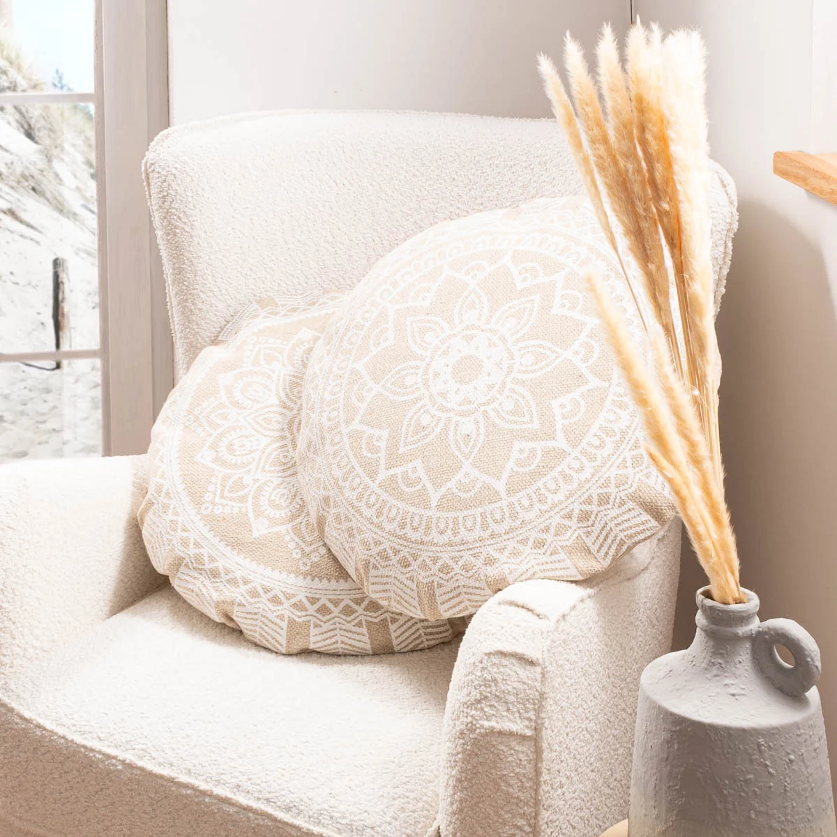 Rundes Mandala-Zierkissen in Creme auf hellem Sessel mit Trockengräsern