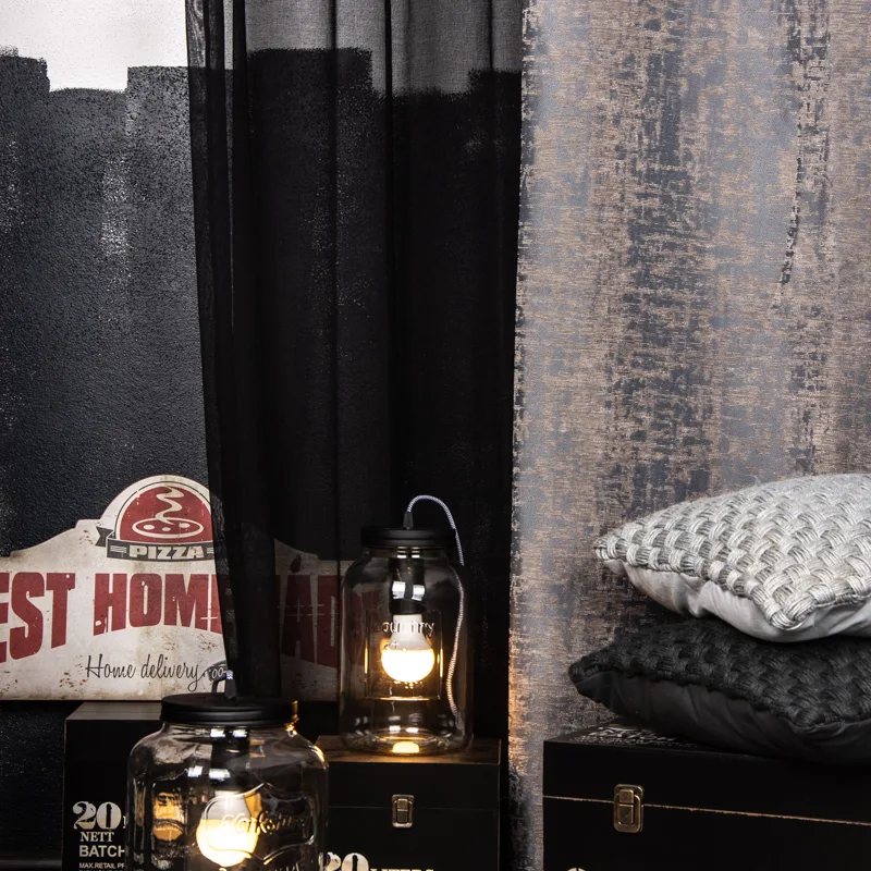 Industrial-Stil mit dunklen Vorhängen, Strickkissen und Laterne auf schwarzen Holzkisten