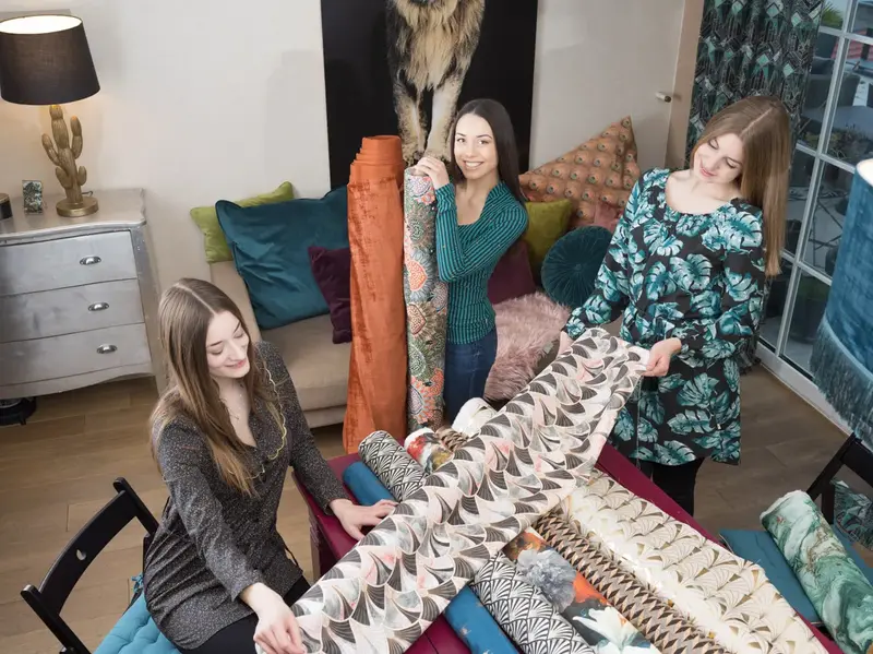 Drei Frauen begutachten Retro-Dekostoffe mit Fächermuster auf einem Tisch