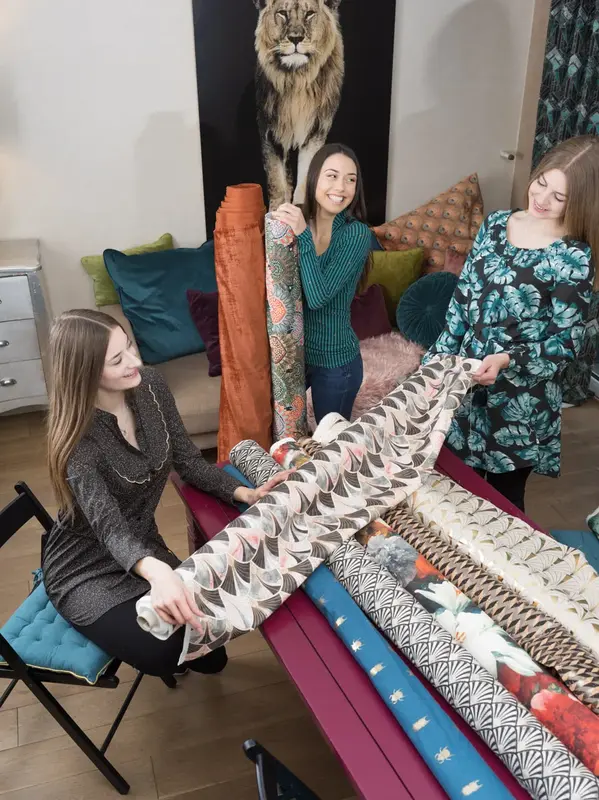 Stoffballen mit Retro-Fächermuster wird ausgerollt, dahinter bunte Dekostoffe