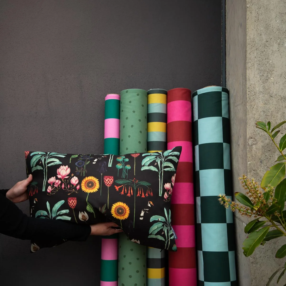 Bunte Dekostoff-Rollen mit Blumenkissen an grauer Wand