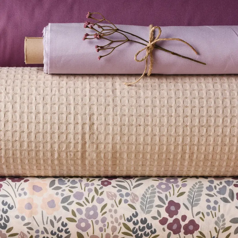 Gestapelte Dekostoff-Rollen in Beige, Flieder und Aubergine mit Struktur- und Blumenmuster