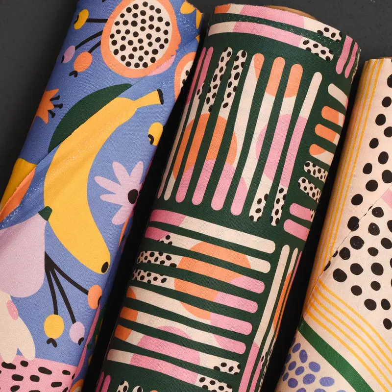 Bunt gemusterte Dekostoffe mit grafischen Prints in Rosa, Gelb und Blau auf dunklem Grund