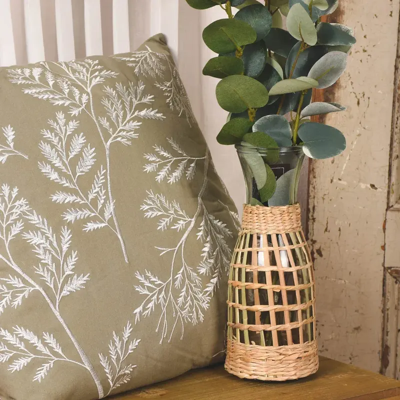 Rattan-Vase mit Eukalyptus neben gr&uuml;nem Kissen mit Zweigmotiv