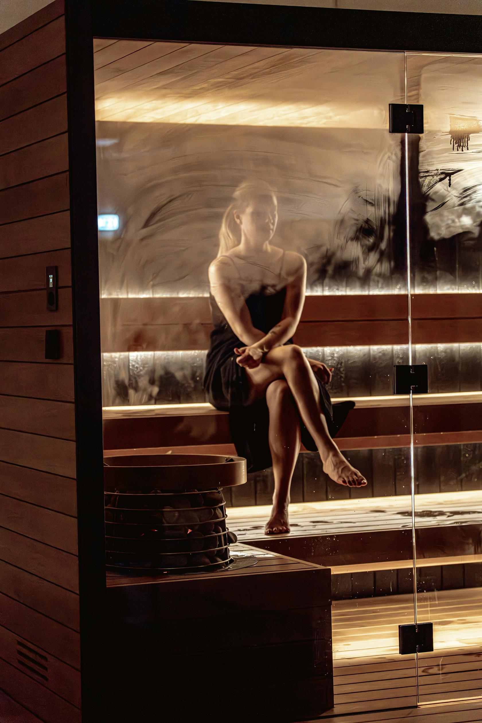 Frau sitzt in der Sauna neben dem Saunaofen mit Steinen