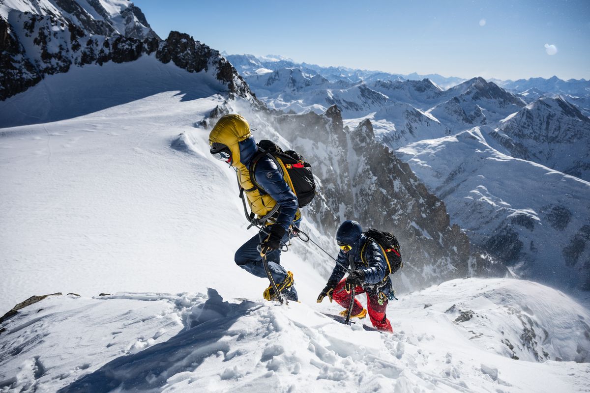 Zwei Bergsteiger mit Steigeisen und Pickel steigen am Seil &uuml;ber einen verschneiten Grat auf