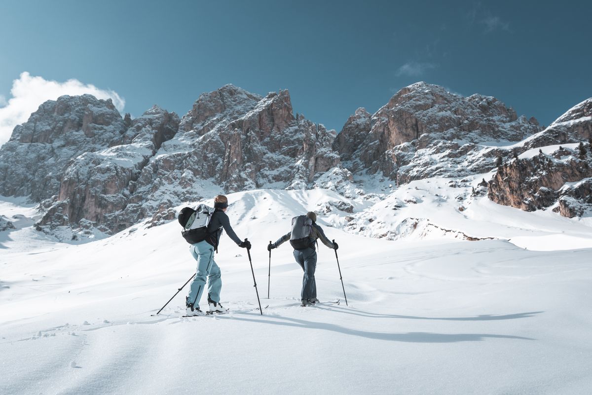 Zwei Skitourengeher mit Rucks&auml;cken im Aufstieg vor Felsgipfeln der Dolomiten