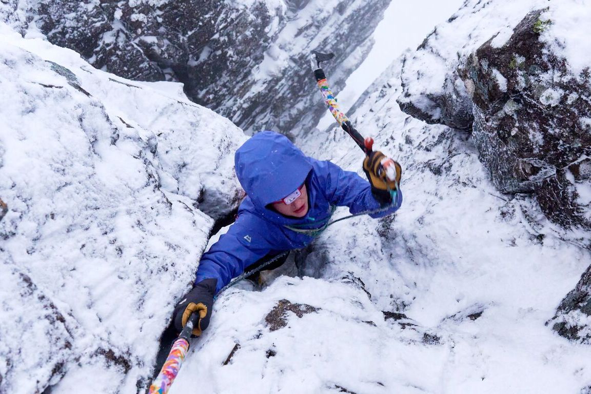 Blick von oben in eine verschneite Felsrinne: Aufstieg mit zwei Eisger&auml;ten in einer blauen Hardshelljacke mit Kapuze