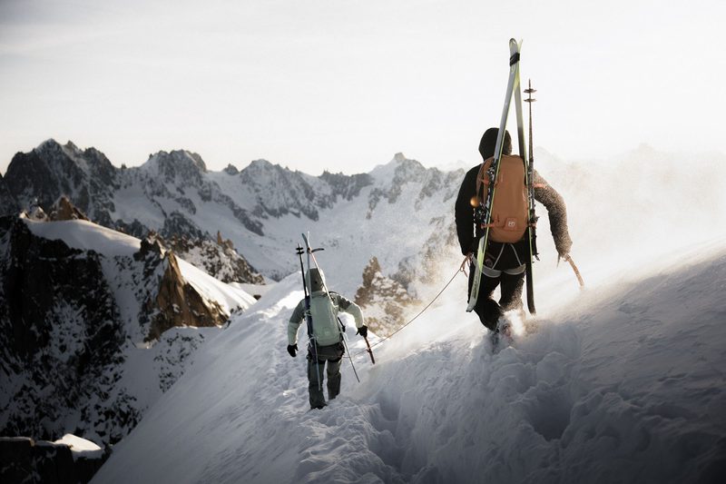 Zwei Skitourengeher mit Ski am Rucksack steigen &uuml;ber einen verschneiten Grat auf