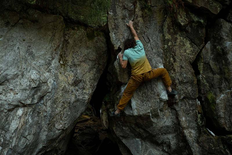 Boulderer in ockerfarbener Kletterhose an einem Felsblock im Wald
