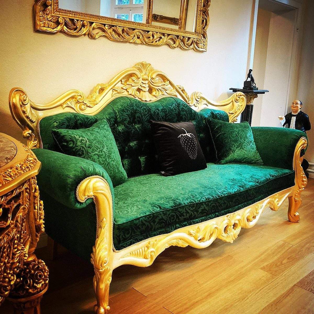 Casa Padrino Erfahrung: Barock-Sofa mit grünem Samtbezug und vergoldetem Schnitzrahmen unter einem goldenen Wandspiegel