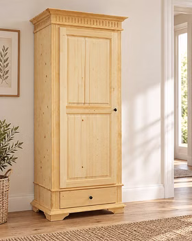 Landhaus Dielenschrank 90x205x58cm DAHLIA Fichte natur geölt Massiver Landhausschrank DAHLIA aus hellem Fichtenholz mit einer geschlossenen Kassettentür, einer Schublade und dekorativem Kranzprofil, platziert in einem hellen Wohnraum.