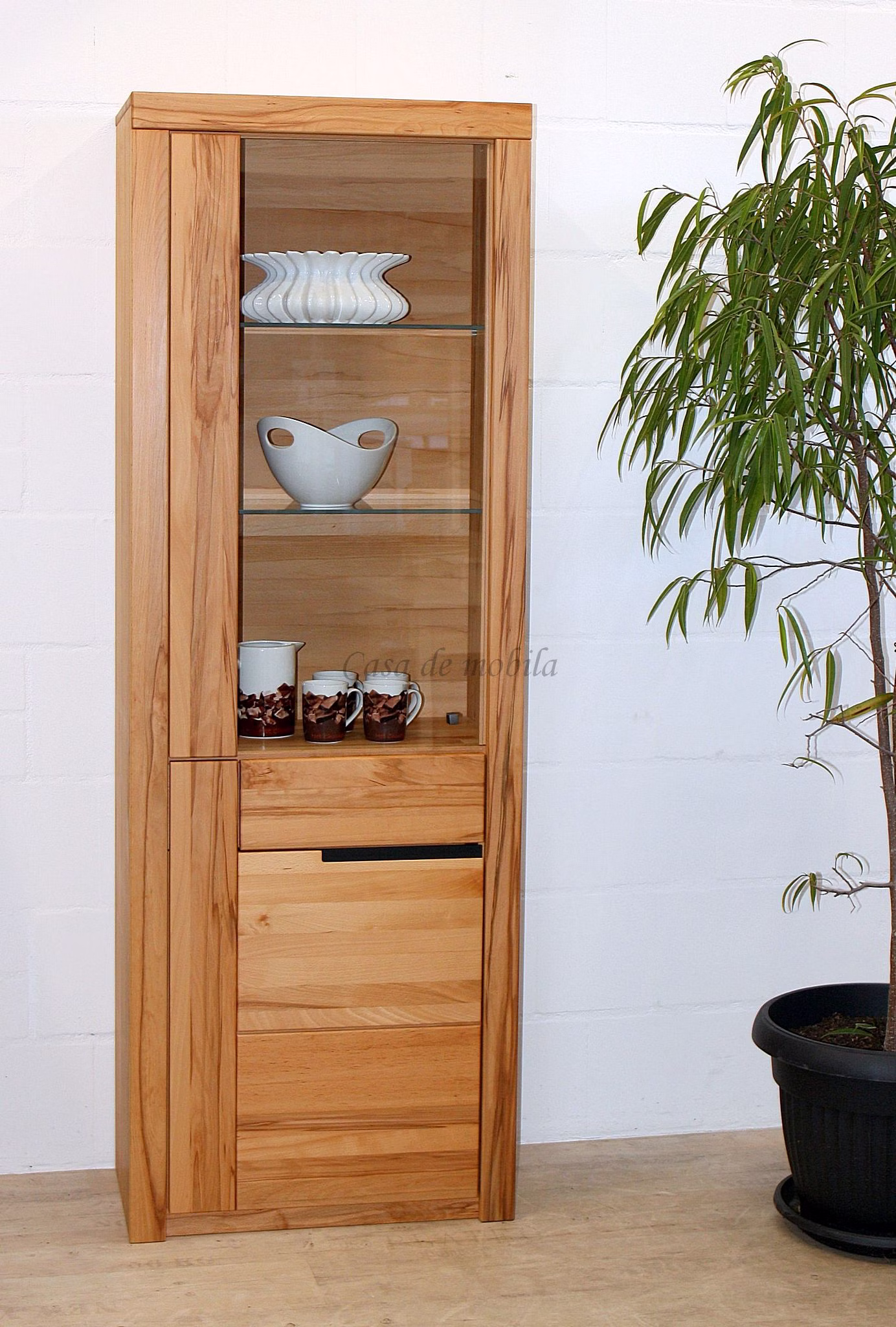 Schmale Holzvitrine mit Geschirr Schmale Holzvitrine mit Geschirr hinter Glas über einem geschlossenen Unterschrank.