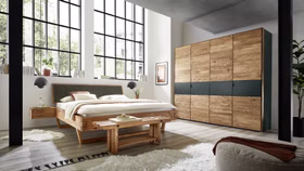 schlafzimmer-balkenbett-woodstock-620-anthrazit-rustikal. Rustikales Balkenbett WOODSTOCK 620 mit anthrazitfarbenem Kopfteil in einem modern eingerichteten Schlafzimmer.